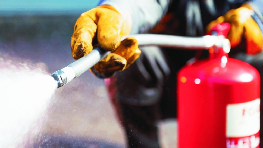 Fire Marshal Training: Person using fire extinguisher wearing protective equipment.