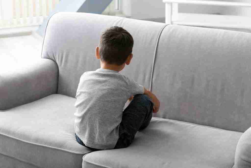 A young boy at risk of ligature sat facing away on a grey sofa. Ligature Awareness Training