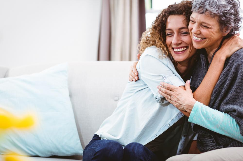 Personal and Pressure Care, young woman hugging mother on sofa.