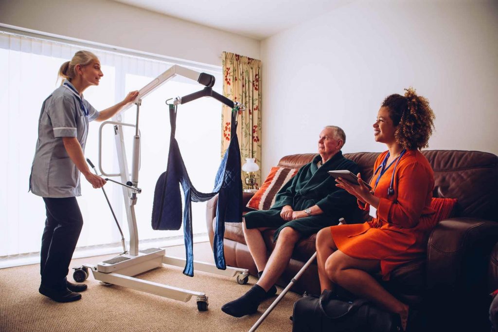 Moving People Safely Hoist, two care workers with elderly man and hoist.