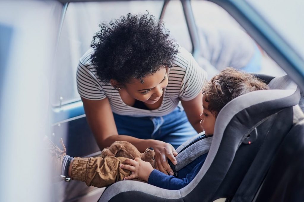Therapeutic Parenting, young woman strapping child into child seat in car.