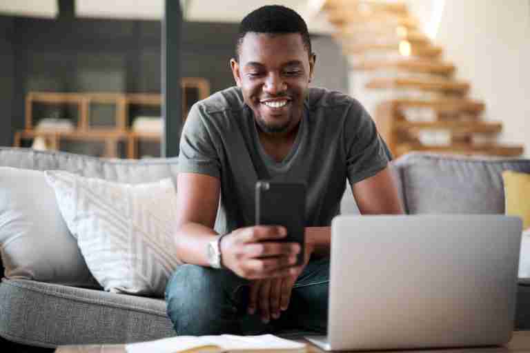 Contact Us, man using phone and laptop sat on sofa