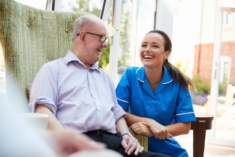 Carer smiling with an older man in a dementia care setting, showing positive and compassionate support.